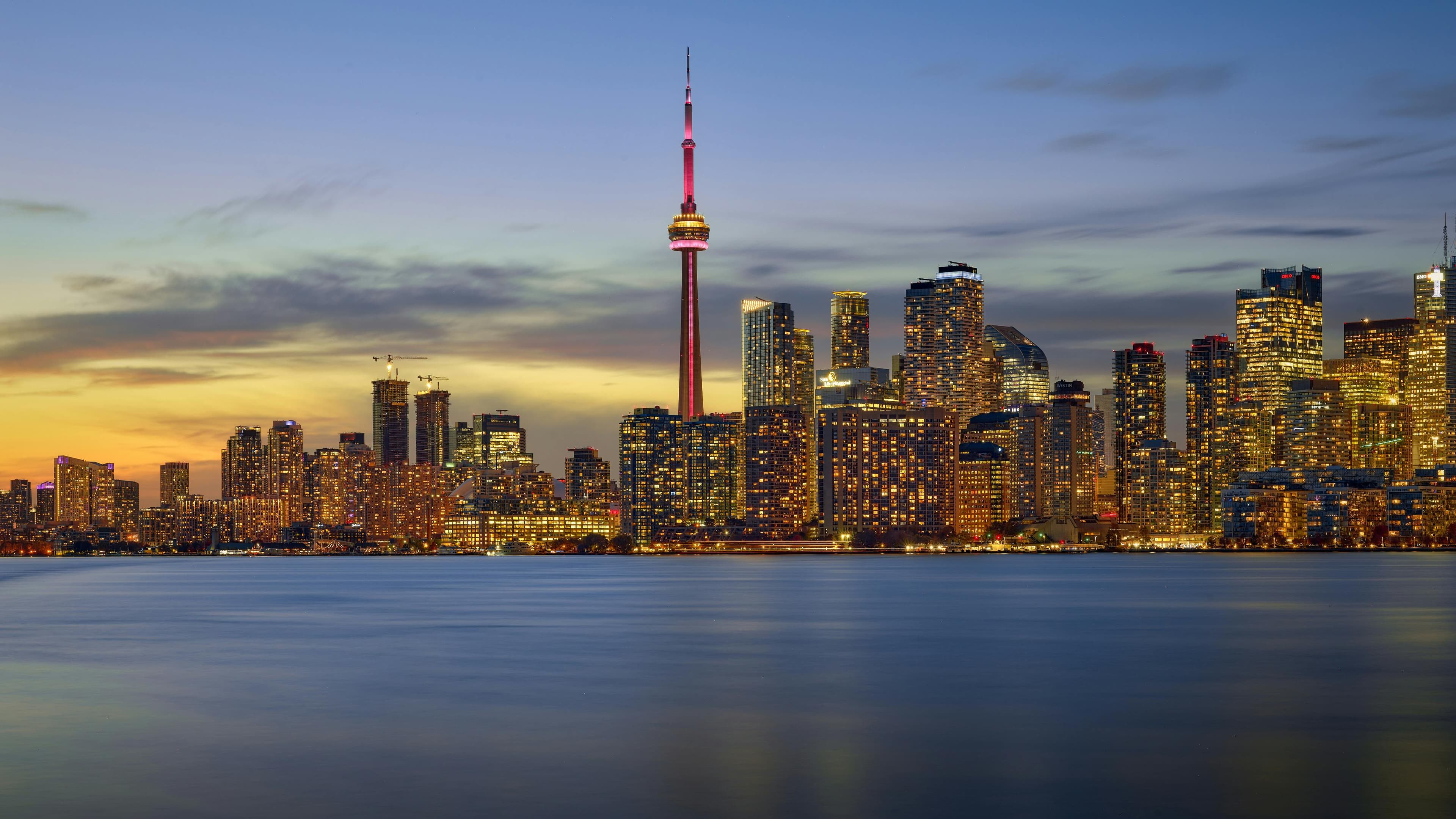 The Toronto skyline at dusk across Lake Ontario, the CN Tower lit above the downtown towers