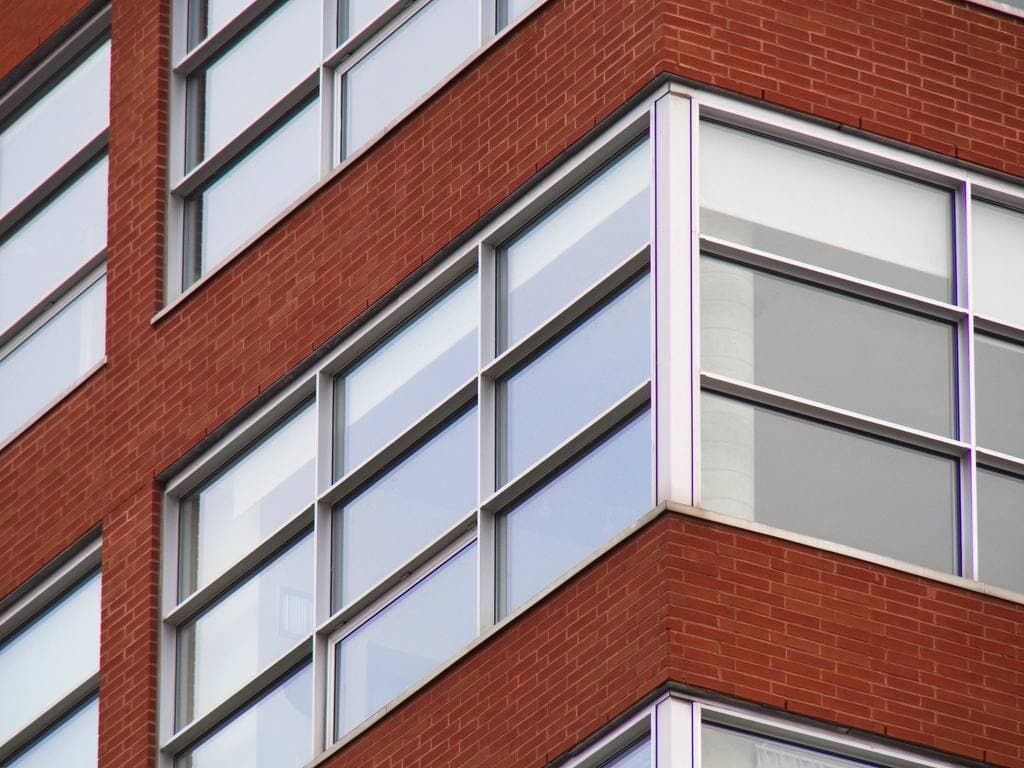 Close-up of the corner of a modern red-brick mid-rise building with rows of large white-framed windows.