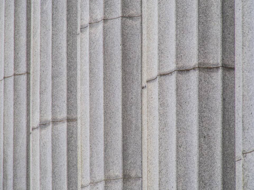 Close-up of fluted pale stone columns on a classical building facade, their grooved surfaces lit by soft even daylight.