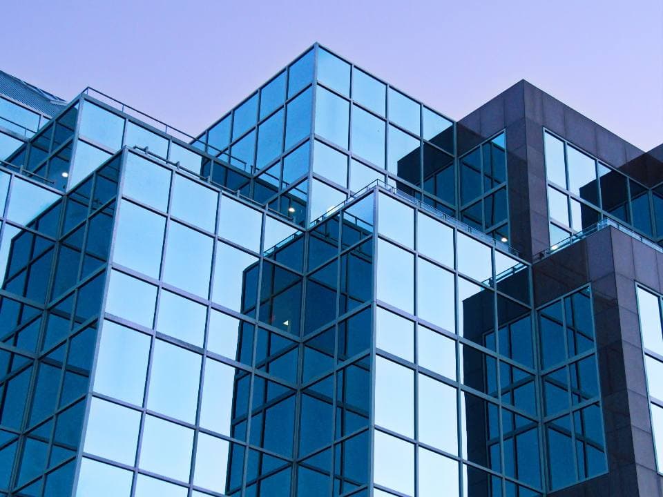Angular blue glass curtain wall of a modern mid-rise office building catching a pale lavender sky at dusk.