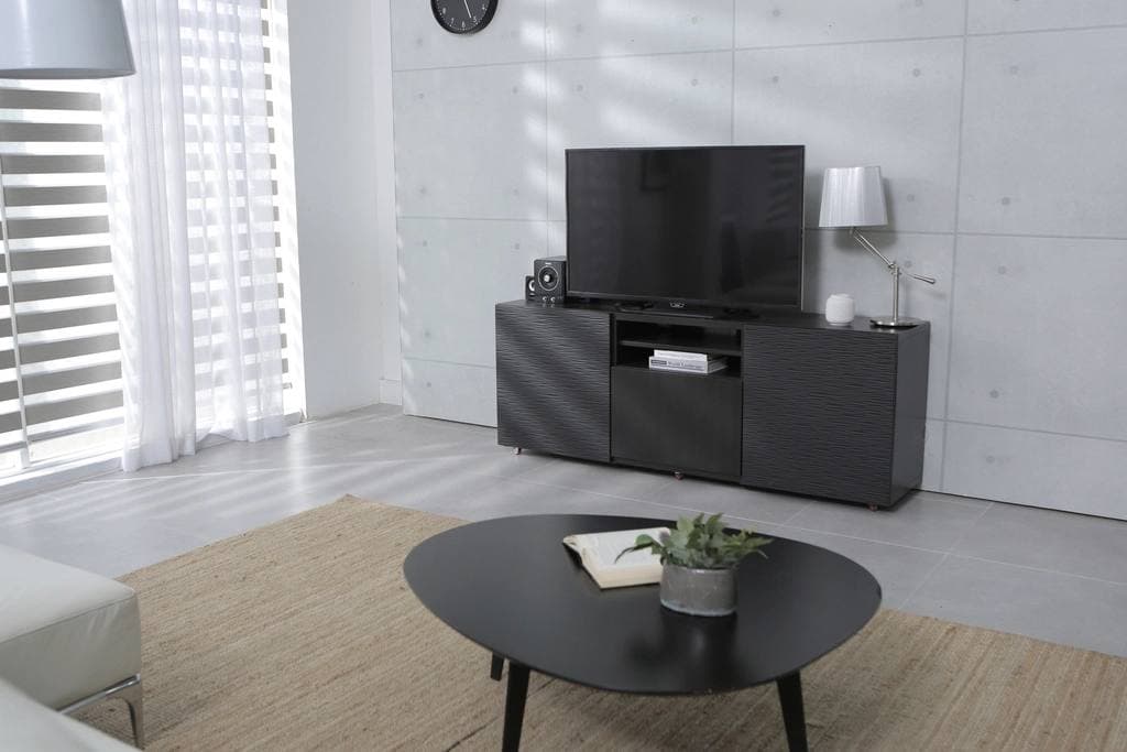 A pale grey living room with a low black media unit and television, a rounded coffee table holding an open book and a small plant, and a woven rug.