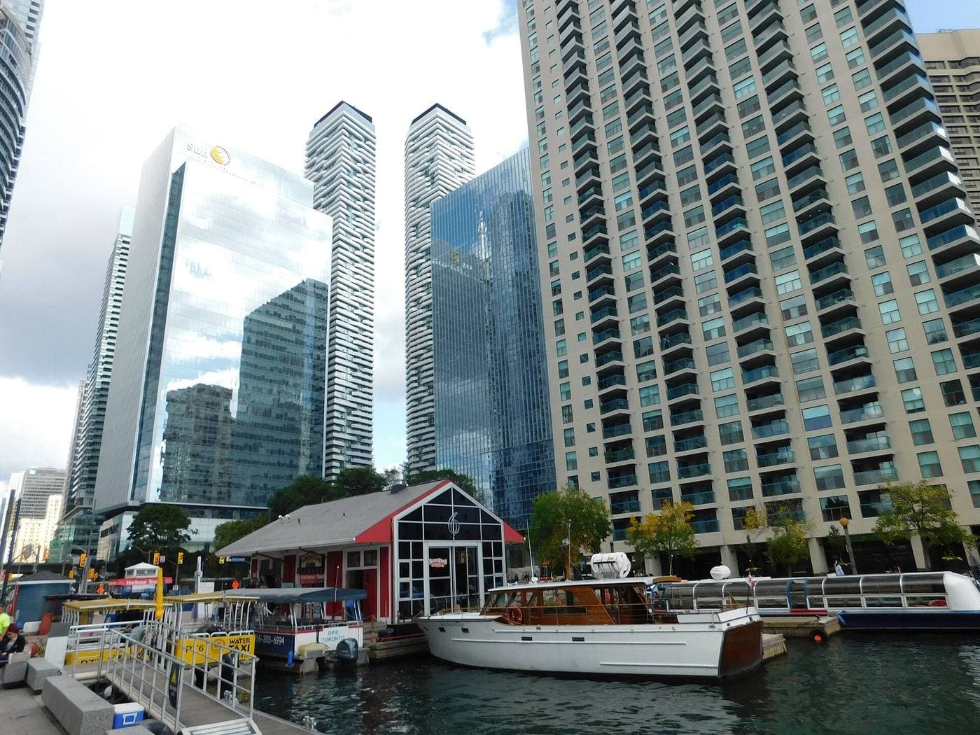 Water taxis and a wooden cruiser moored at Toronto's harbourfront, below glass condominium and office towers at York Quay.