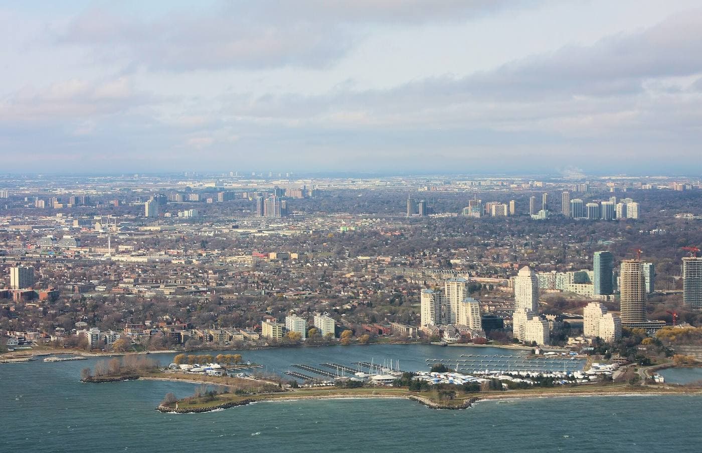 Aerial view of the Lake Ontario shoreline at Humber Bay, with a marina, clustered waterfront condominium towers under construction and low-rise neighbourhoods inland.