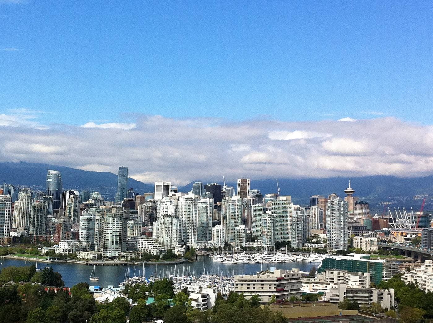Downtown Vancouver's glass condo towers and Harbour Centre rise beyond a marina packed with sailboats, with the North Shore mountains behind.