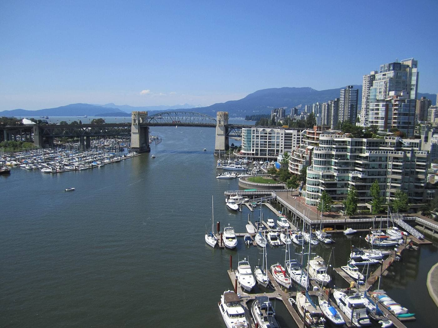 Burrard Street Bridge over False Creek, with packed sailboat marinas below and glass condo towers rising toward the North Shore mountains.