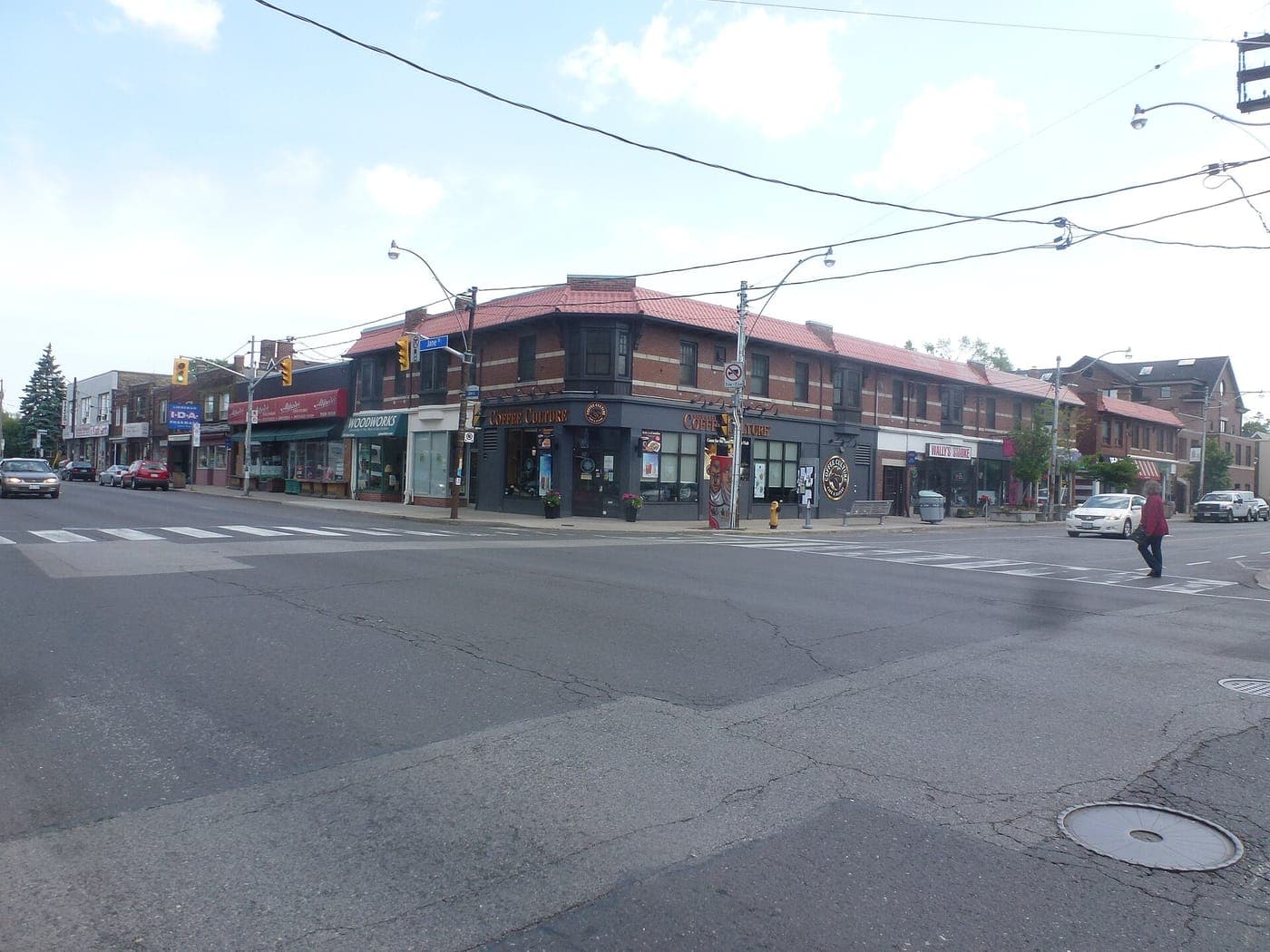 Quiet street corner with a two-storey brick building with a red tile roof housing a café and shops, traffic lights, crosswalks and a pedestrian crossing