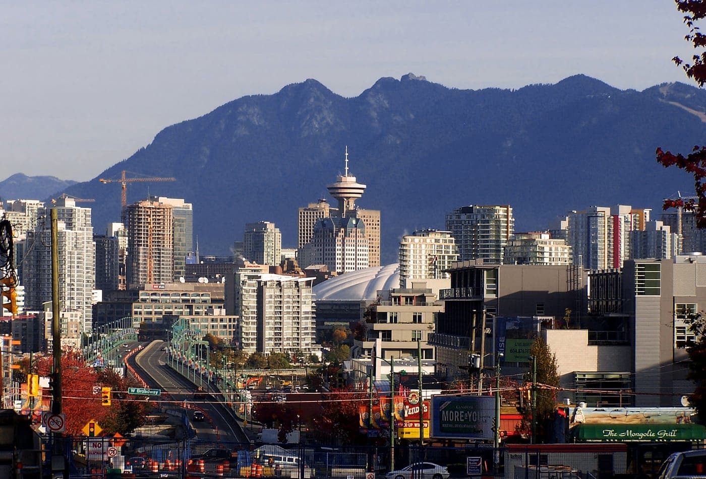Vancouver skyline with Harbour Centre tower and BC Place dome in front of the North Shore mountains, seen from West Broadway with the Cambie Bridge leading downtown.