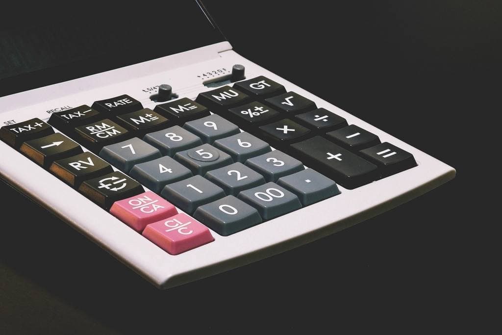 Close-up of a white desktop calculator angled across a dark surface, showing grey number keys, black function keys and two pink clear buttons.