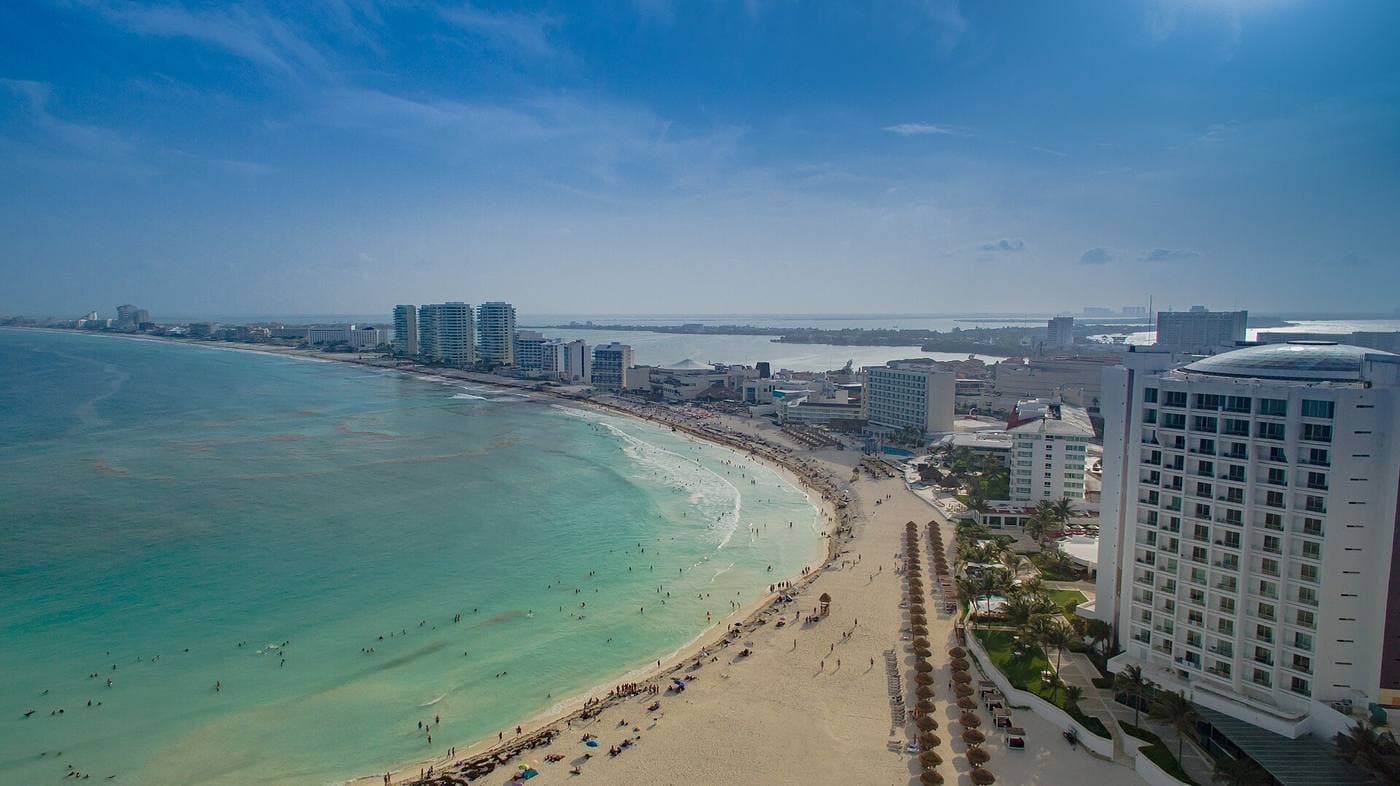 Aerial view along Cancún's hotel zone, a ribbon of white-sand beach and turquoise sea lined with resorts.