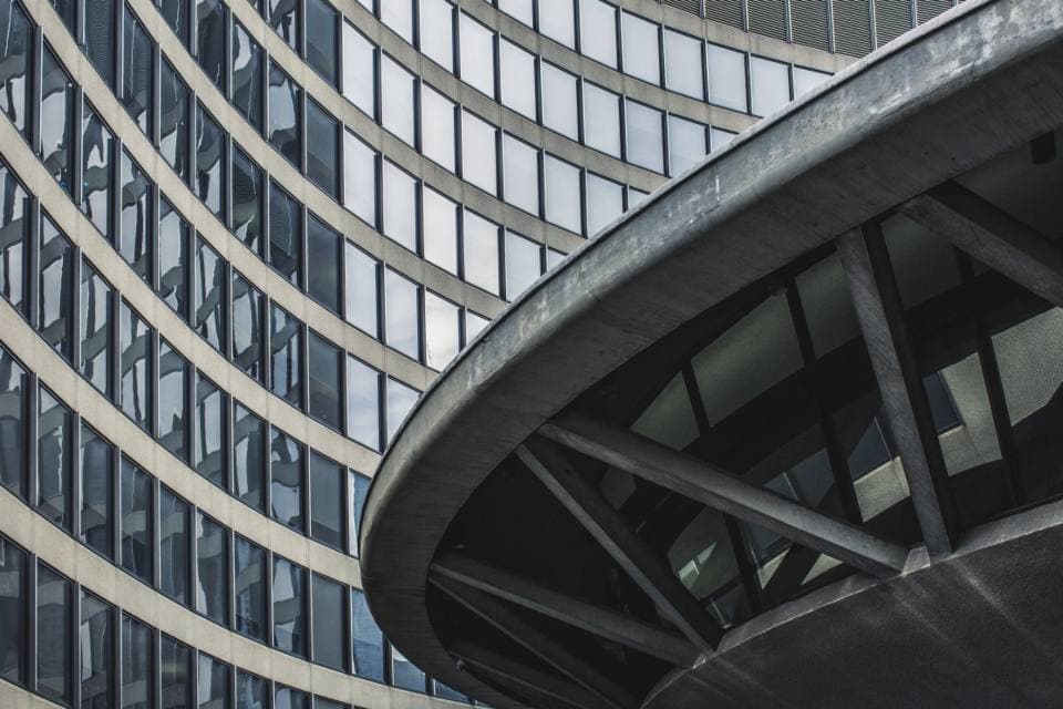 Curved grid of windows on a modern office tower rising behind a sweeping concrete and steel canopy.