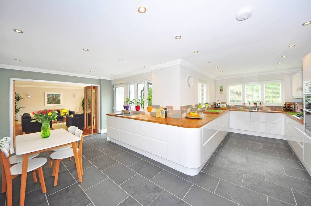 A spacious open-plan kitchen and dining area with white gloss cabinets, wooden worktops and a grey tiled floor.