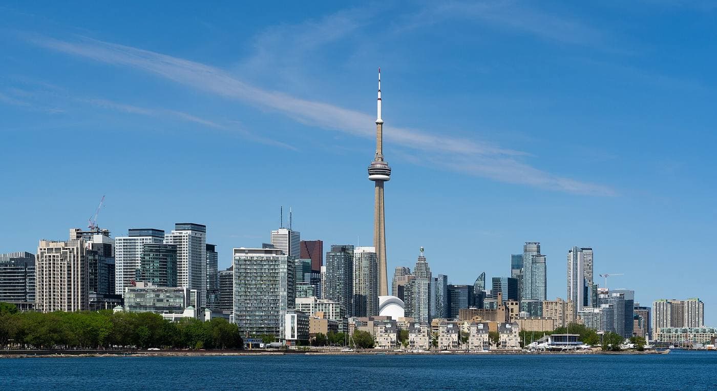 The CN Tower and a broad wall of downtown Toronto office and condo towers seen across the blue water of the inner harbour on a clear day.