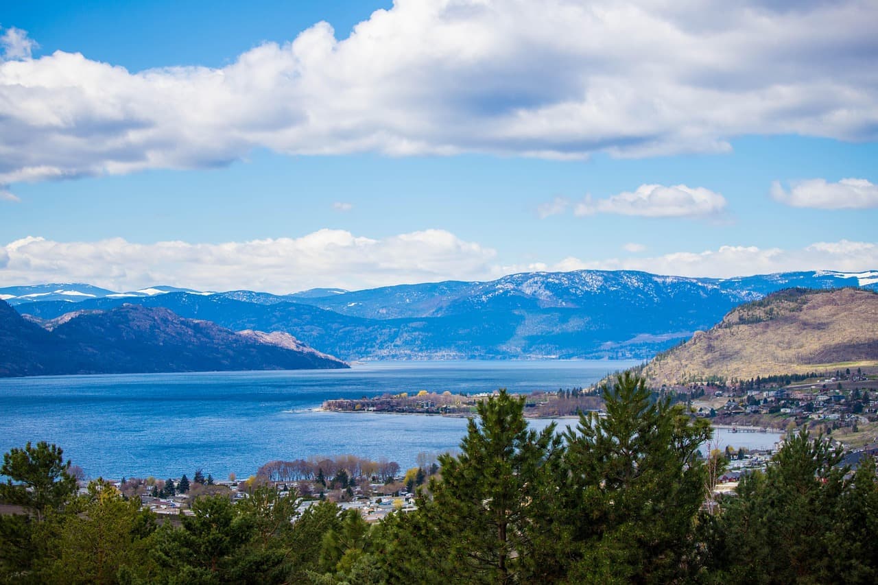 Okanagan Lake seen from the hillside above, with homes along the shoreline and snow still on the far ridges (The Okanagan, British Columbia)